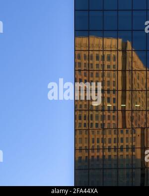 Dividi la prospettiva di un cielo blu chiaro e lo specchio esterno in vetro di un moderno grattacielo che riflette un altro edificio nelle vicinanze Foto Stock