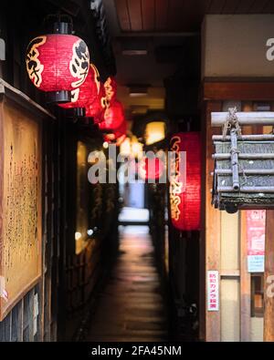 Fuoco selettivo sulla prima di una linea di rosso lanterne di carta che conducono in un vicolo coperto scarsamente illuminato Centro di Osaka Foto Stock