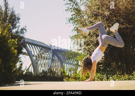 donna che fa un handstand in strada contro un ponte Foto Stock