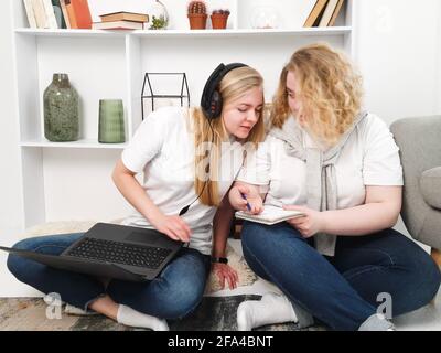 due donne che studiano seduto sul pavimento con il laptop e. cuffie Foto Stock