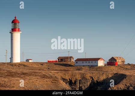 Un faro bianco e rosso a forma di cilindro in cemento con un grande luce di vetro verde nella parte superiore della torre rossa su una scogliera che si affaccia sul cielo blu Foto Stock