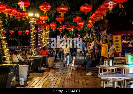 Sanya China, 25 marzo 2021: Vicolo della spiaggia di Dadonghai di notte con ristorante e terrazze bar con persone nella città di Sanya Hainan isola Cina Foto Stock