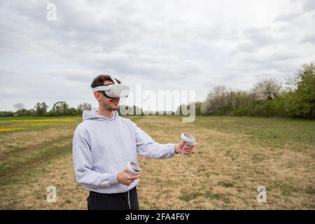 Un ragazzo gioca con il visore VR e i controller in un prato all'aperto Foto Stock