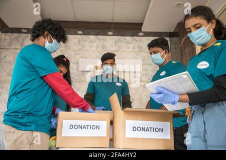 Focus sulla ragazza di fronte, gruppo di volontari impegnati a lavorare organizzando abiti e scatole di donazione durante il coronavirus covid-19 pandemic lockdown - concetto Foto Stock