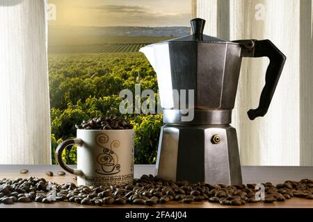 Chicchi di caffè in una tazza e macchina per il caffè italiana un tavolo di legno con campo da caffè visto attraverso una finestra In Brasile Foto Stock