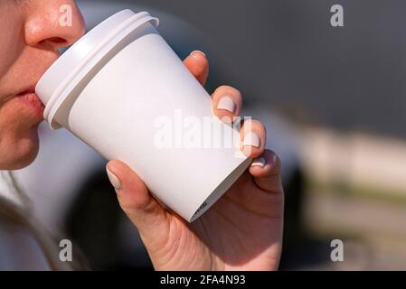 Una donna che tiene una tazza di carta bianca con caffè di bevanda o tè al mattino in una strada della città, tazza bianca di cartone bianco Foto Stock