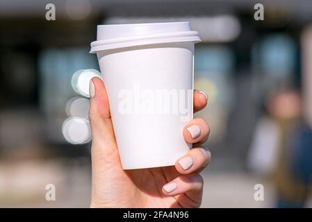 Una donna che tiene una tazza di carta bianca con caffè di bevanda o tè al mattino in una strada della città, tazza bianca di cartone bianco Foto Stock