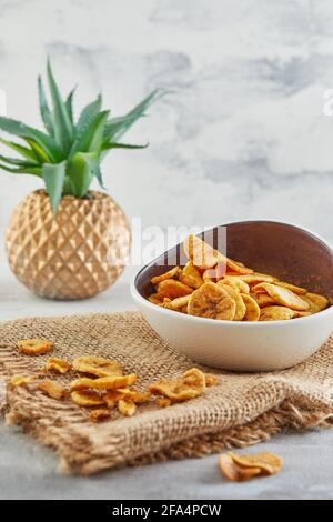 Banana chips cibo sano, frutta secca e patatine vegetali sane, sano vegan snack su burlap e aloe fiore. Foto Stock