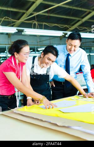 Donna Designer o un marinaio, fogna, lavoratore o responsabile di produzione e proprietario o CEO guardare modello su un tavolo in una fabbrica tessile Foto Stock