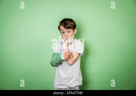 giovane scolaro fresco con braccio rotto e gesso verde del braccio posa davanti a sfondo verde Foto Stock