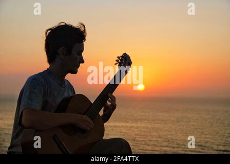 Silhouette di donna che suona la chitarra, alba sul mare in background Foto Stock