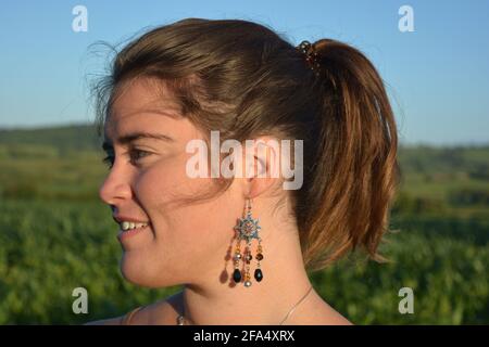Profilo ritratto di bella giovane donna che indossa orecchini, all'aperto, primo piano Foto Stock