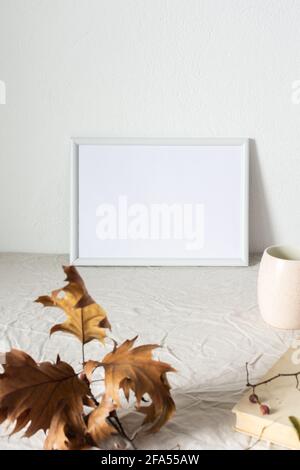 Casa decoratore moccap, quadro vuoto cornice vicino bianco dipinto muro di cemento, rami con foglie secche e libri antichi Foto Stock