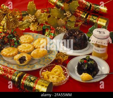 Cibo di Natale tradizionale su sfondo rosso con cracker, torte mince, budino di Natale, burro di brandy e decorazioni Foto Stock