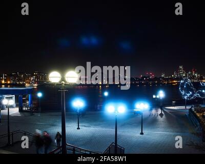 Una vista grandangolare di un paesaggio cittadino londinese notturno, visto da Canary Wharf e con persone che si sfolgorano di movimento per dare vita alla scena. Foto Stock