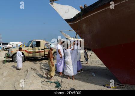 Attività di pesca sulla spiaggia di Shannah, Oman. Uomini che discutono sotto l'arco di un dhow.discus Foto Stock