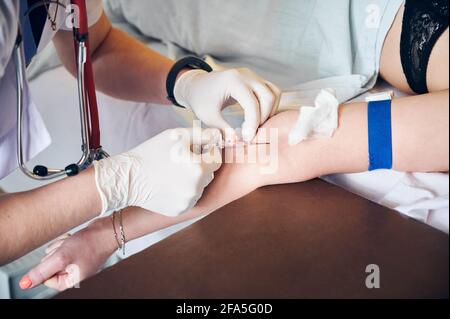 Primo piano delle mani dell'anestesista in guanti sterili iniettando la dose di anestetico. Medico che inserisce l'ago nel braccio del paziente durante l'iniezione del farmaco anestetico prima dell'intervento chirurgico. Concetto di medicina. Foto Stock