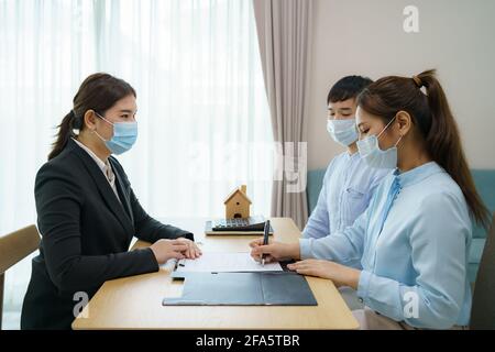 Gli agenti immobiliari della donna asiatica stanno avendo i clienti firmano i contratti per vendere le loro case mentre indossano le maschere per impedire la diffusione di COVID-19. Foto Stock