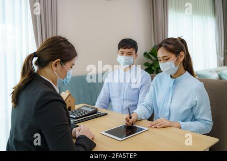 Gli agenti immobiliari della donna asiatica stanno avendo i clienti firmano i contratti vendere le loro case in tablet digitale indossando marchi per evitare la diffusione di Foto Stock