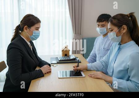 Gli agenti immobiliari della donna asiatica stanno avendo i clienti firmano i contratti vendere le loro case in tablet digitale indossando marchi per evitare la diffusione di Foto Stock