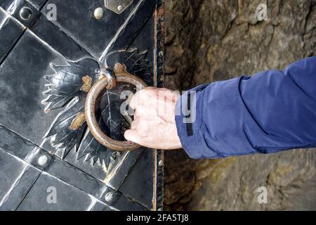 L'uomo apre un'antica porta in metallo decorata con elementi in ferro battuto. Antico castello con manico in ferro a forma di anello. Primo piano. Messa a fuoco selettiva. Foto Stock