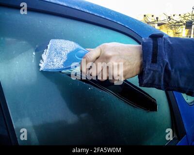 L'uomo raschia il gelo con un raschietto di plastica dal finestrino  laterale di un'automobile