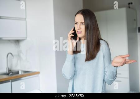 Conversazione telefonica sgradevole. Una giovane donna parla sullo smartphone con irritata espressione del viso, gestendo emotivamente Foto Stock