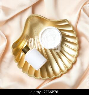 Vasetto di crema idratante e lozione corpo su conchiglia dorata su seta color pesca. Disposizione piatta, vista dall'alto. Foto Stock