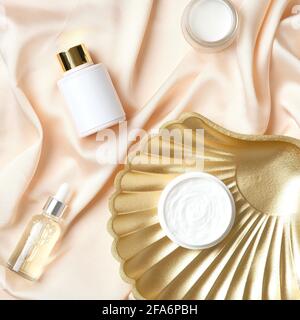 Set di prodotti di bellezza di lusso e seaschell dorato su sfondo di seta color pesca. Piatto, vista dall'alto crema corpo, lozione, siero. Foto Stock