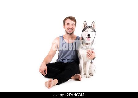 Giovane uomo bearded che si stese con il suo cane Husky. Hipster maschio che indossa tank top grigio chiaro che passa del tempo di qualità con un amico animale domestico a quattro zampe Foto Stock