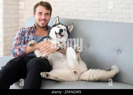 Giovane uomo bearded che si stese con il suo cane Husky. Hipster maschio con camicia a scacchi in flanella e canotta grigia trascorrere del tempo di qualità con quattro l. Foto Stock