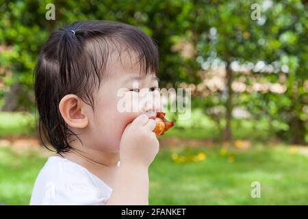 Closeup adorabile ragazza asiatica (tailandese) godere di mangiare il suo pranzo nel parco, bambino mangiare pollo fritto su sfondo verde sfocato natura Foto Stock