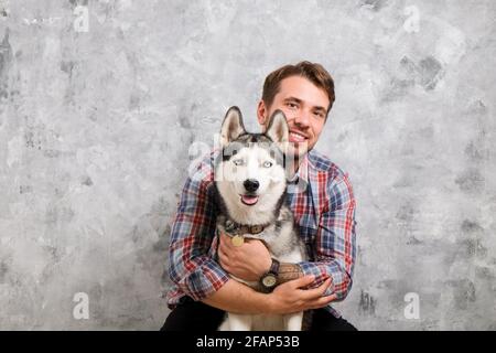 Giovane uomo bearded che si stese con il suo cane Husky. Hipster maschio con camicia a scacchi in flanella e canotta grigia trascorrere del tempo di qualità con quattro l. Foto Stock