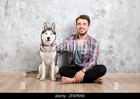 Giovane uomo bearded che si stese con il suo cane Husky. Hipster maschio con camicia a scacchi in flanella e canotta grigia trascorrere del tempo di qualità con quattro l. Foto Stock