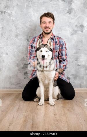 Giovane uomo bearded che si stese con il suo cane Husky. Hipster maschio con camicia a scacchi in flanella e canotta grigia trascorrere del tempo di qualità con quattro l. Foto Stock