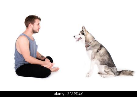 Giovane uomo bearded che si stese con il suo cane Husky. Hipster maschio che indossa tank top grigio chiaro che passa del tempo di qualità con un amico animale domestico a quattro zampe Foto Stock