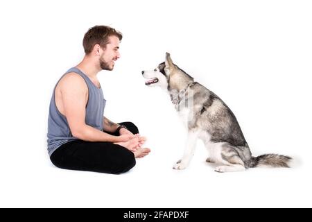 Giovane uomo bearded che si stese con il suo cane Husky. Hipster maschio che indossa tank top grigio chiaro che passa del tempo di qualità con un amico animale domestico a quattro zampe Foto Stock