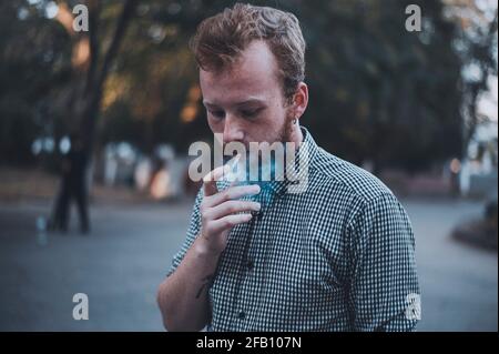 L'uomo giovane ed elegante fuma nel parco. Foto Stock