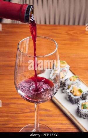 Primo piano di bicchiere di vino rosso e panini di sushi con semi di sesamo su un piatto bianco Foto Stock