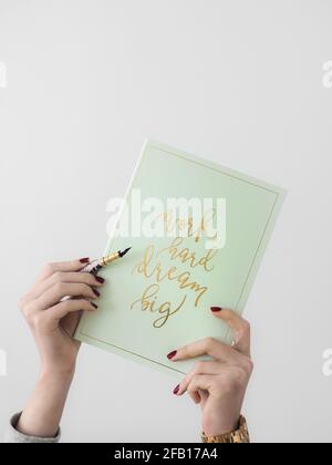 Immagine verticale di mani femminili che tengono un notebook verde con una citazione e una penna ispiratrici Foto Stock