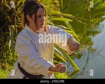 Messa a fuoco superficiale di una giovane donna ispanica adulta che la pratica karate si muove all'aperto accanto ad un lago Foto Stock