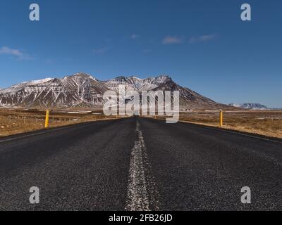 Vista mozzafiato della strada vuota e diritta (Route 54) con una prospettiva decrescente sulla penisola di Snæfellsnes, Islanda occidentale con aspre montagne innevate. Foto Stock
