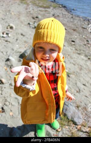 Un ragazzo dai capelli lonesti in un impermeabile giallo, un cappello giallo, contiene un ladybug Foto Stock