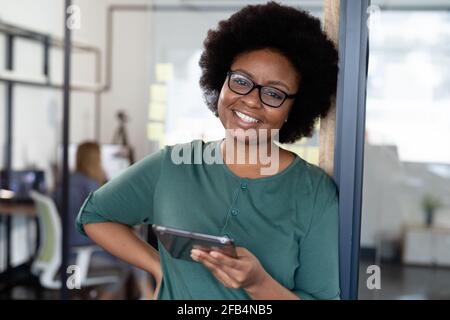 Ritratto di una donna d'affari afro-americana che tiene un tablet digitale e sorride Foto Stock