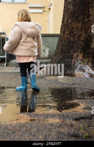 Vista posteriore di una ragazza in stivali di gomma che cammina dentro un puddle Foto Stock
