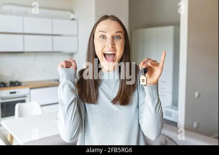 Eccitato giovane donna felice tiene la chiave di nuova casa, guarda la macchina fotografica e grida estatica, ragazza stupita celebra il trasferimento nel proprio appartamento, l'acquisto di una proprietà, urlando felicemente Foto Stock