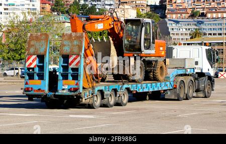 Un scavatore meccanico caricato su un rimorchio del camion nel parcheggio del randello di calcio Santander Santander Cantabria Spagna Sunny primavera mattina Foto Stock