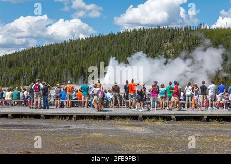 Yellowstone National Park, Montana, USA - Luglio 15 2018: Visitatori che guardano l'eruzione dell'Old Faithful Geyser con la sua acqua bollente. Foto Stock