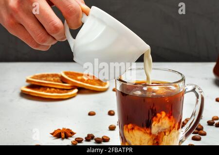 La mano umana versa la crema in una tazza trasparente con caffè, primo piano. Foto Stock