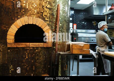 Kuwait City - Kuwait: 10 aprile 2021: Il forno della pizza desidera esterno lucido vicino in cucina con lo chef filippino che indossa la maschera Foto Stock